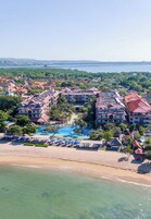 An aerial view of a resort with multiple buildings, a large swimming pool, and a beach.