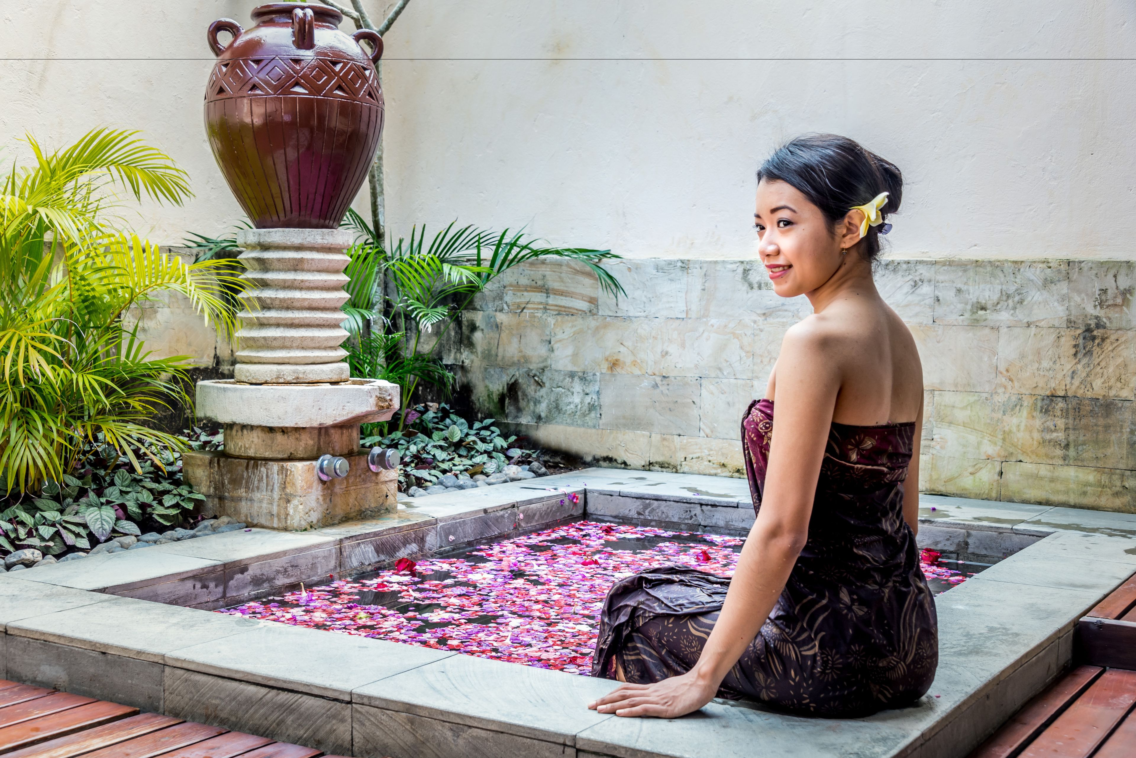 Una mujer sentada junto a una fuente decorativa con base de piedra y un gran jarro.