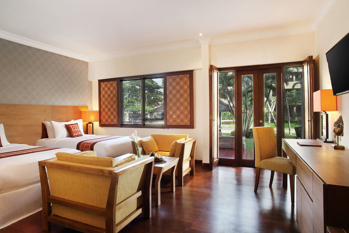 A hotel room with two beds, a sitting area with chairs, a desk, and a TV.