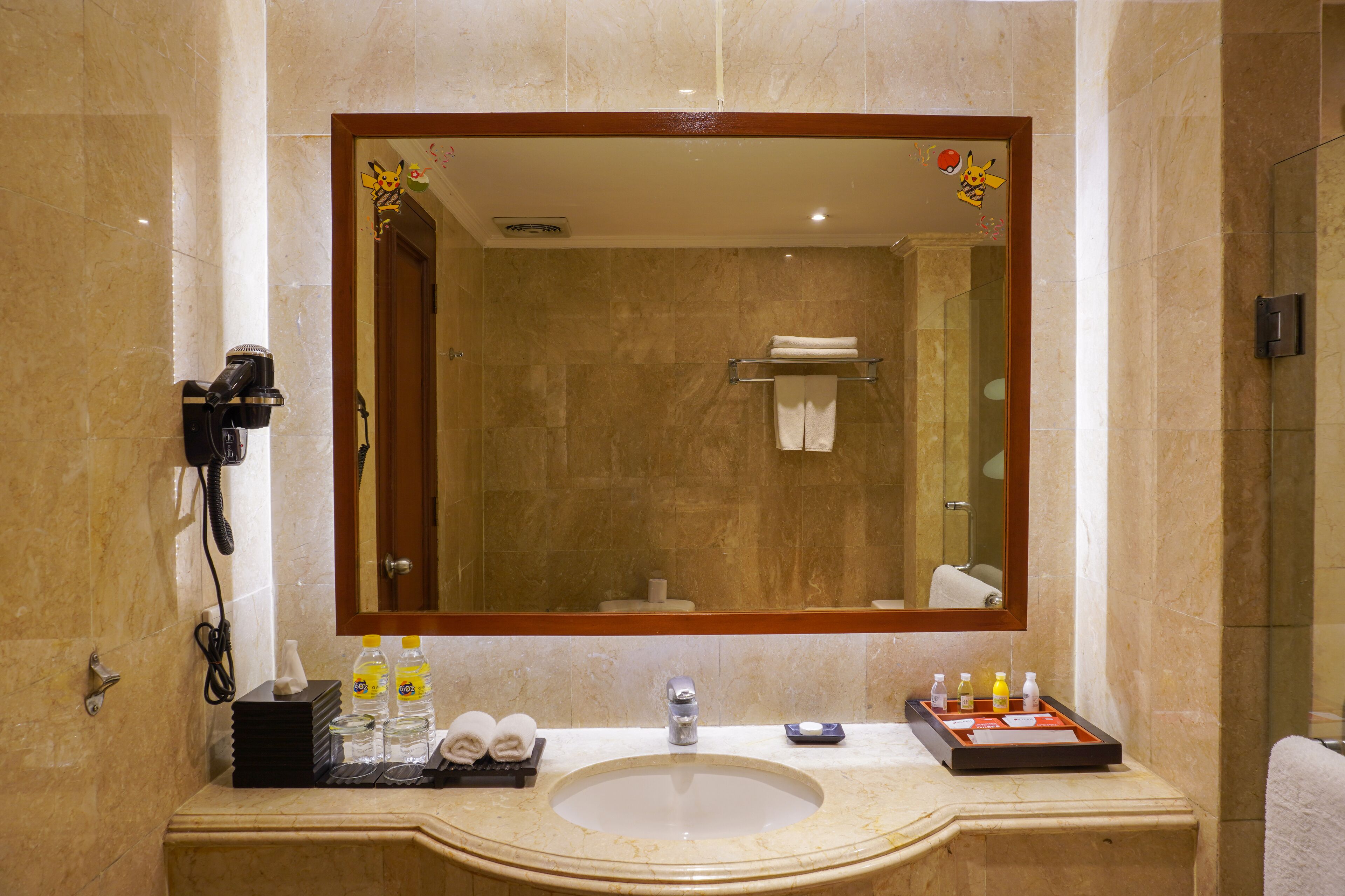 Une salle de bain avec un grand miroir, un lavabo et un sèche-cheveux fixé au mur.
