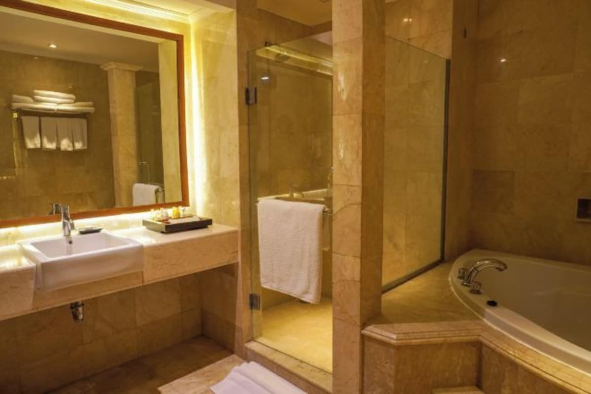 Un baño moderno con un espejo grande, dos lavamanos, una bañera y una zona de ducha con paredes de vidrio.