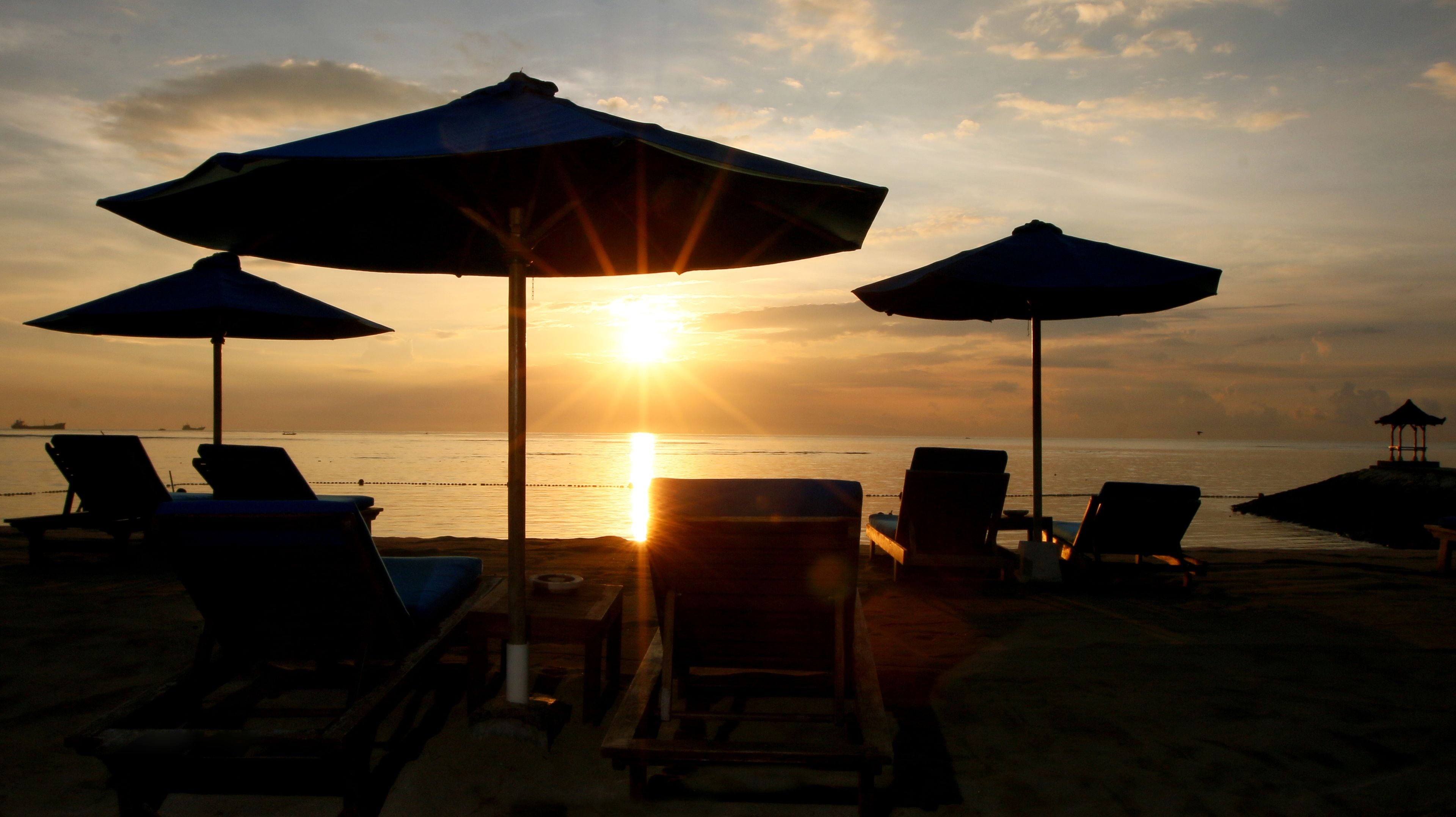 A beach scene with sun umbrellas and lounge chairs facing the ocean at sunset.