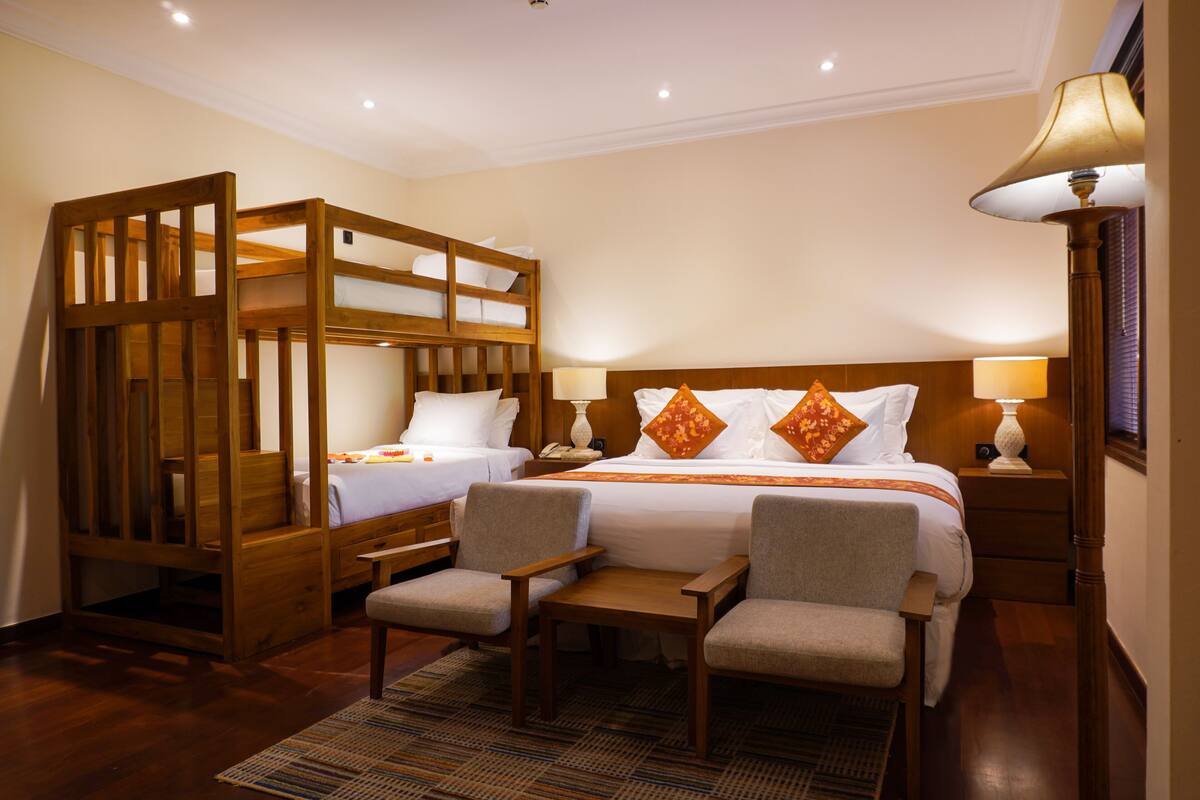 A hotel room with a bunk bed, two armchairs, a small table, and a bedside lamp.