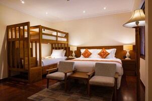 A hotel room with a bunk bed, two armchairs, a small table, and a bedside lamp.