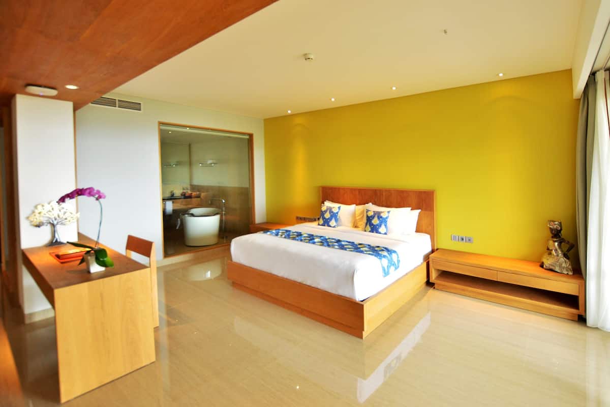 A modern hotel room with a large bed, a wooden desk, and a bathroom visible through an open door.