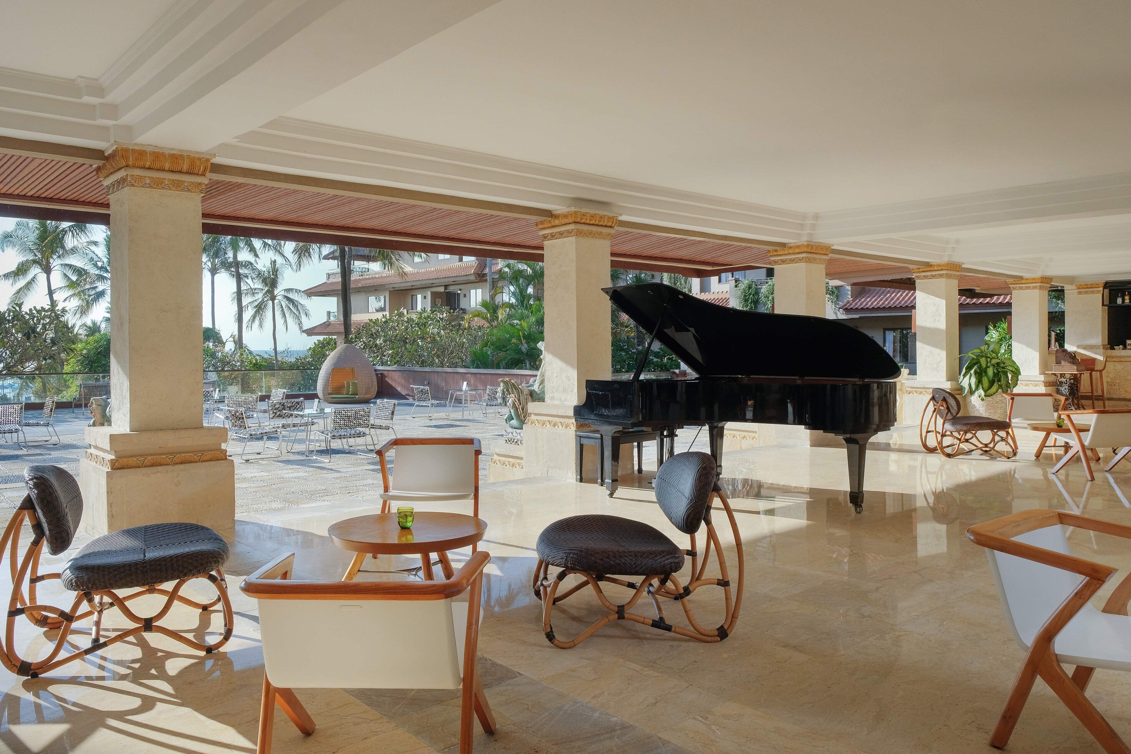 A spacious outdoor lounge area with a grand piano, comfortable seating, and a view of palm trees and buildings.