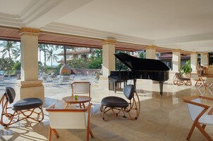 A spacious outdoor lounge area with a grand piano, comfortable seating, and a view of palm trees and buildings.