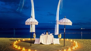 Disposición para comer frente al mar con una mesa redonda, dos sombrillas y un círculo de luces.