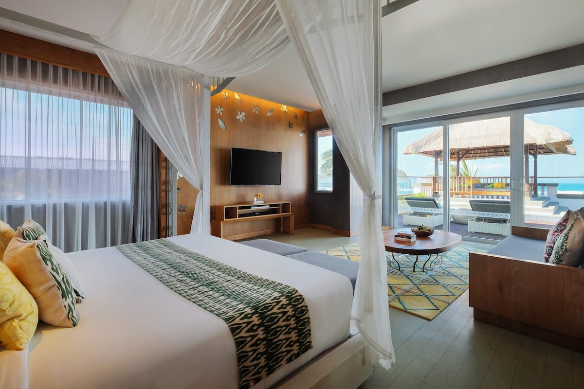 A spacious hotel room with a large bed, a TV, a balcony with a view of the ocean, and a dining area.