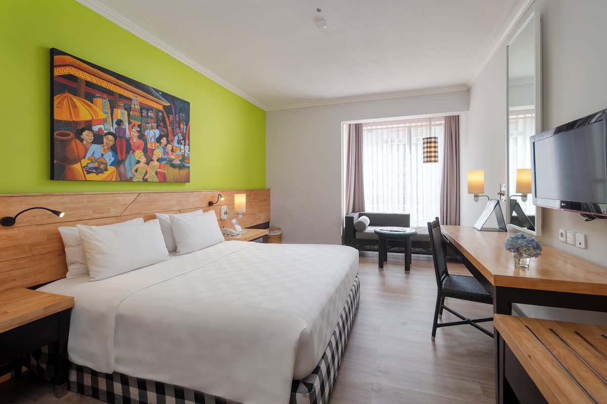 Een hotelkamer met een groot bed, een bureau, een stoel, een televisie en een schilderij aan de muur.