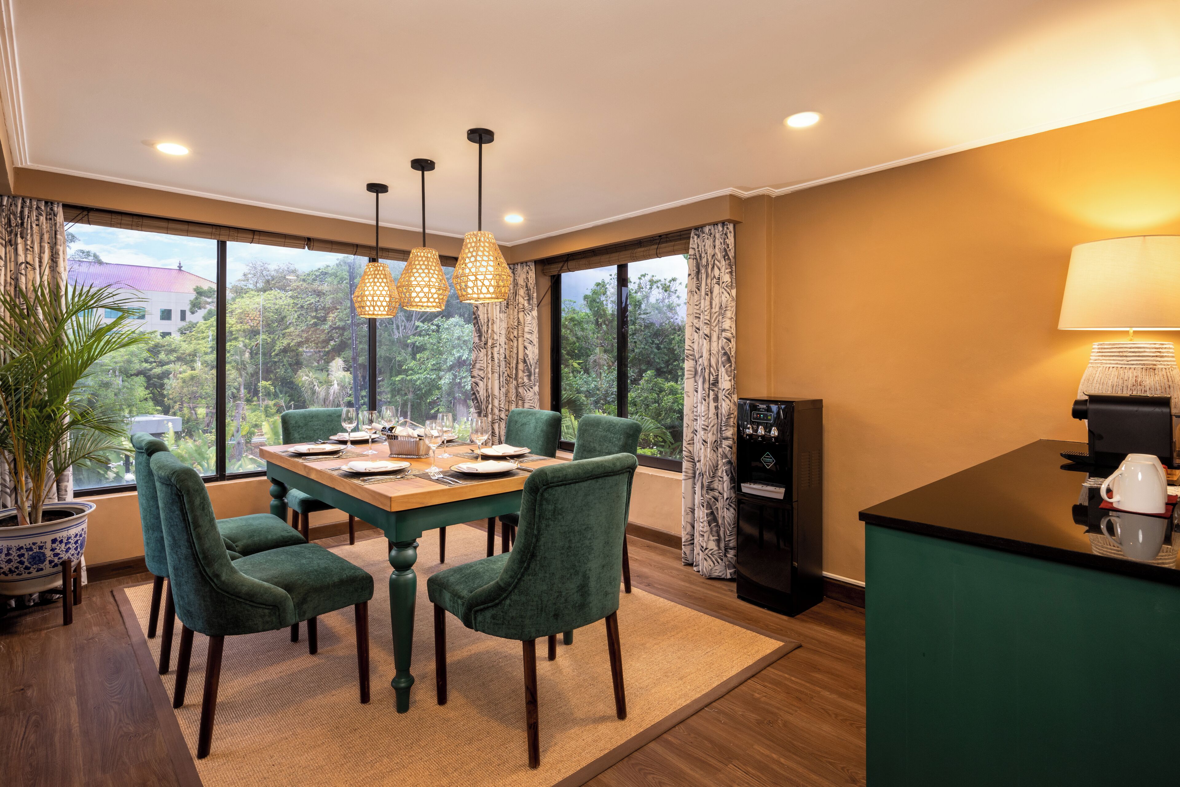 A dining area with a wooden table, green upholstered chairs, and hanging pendant lights.
