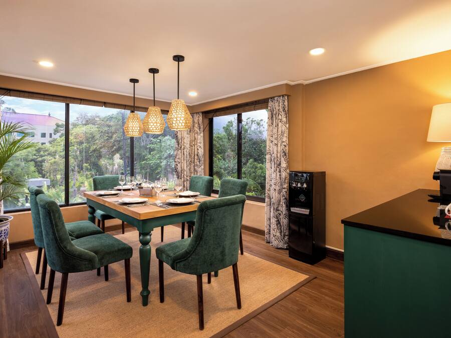 Comedor con mesa de madera, sillas tapizadas en verde y lámparas colgantes.
