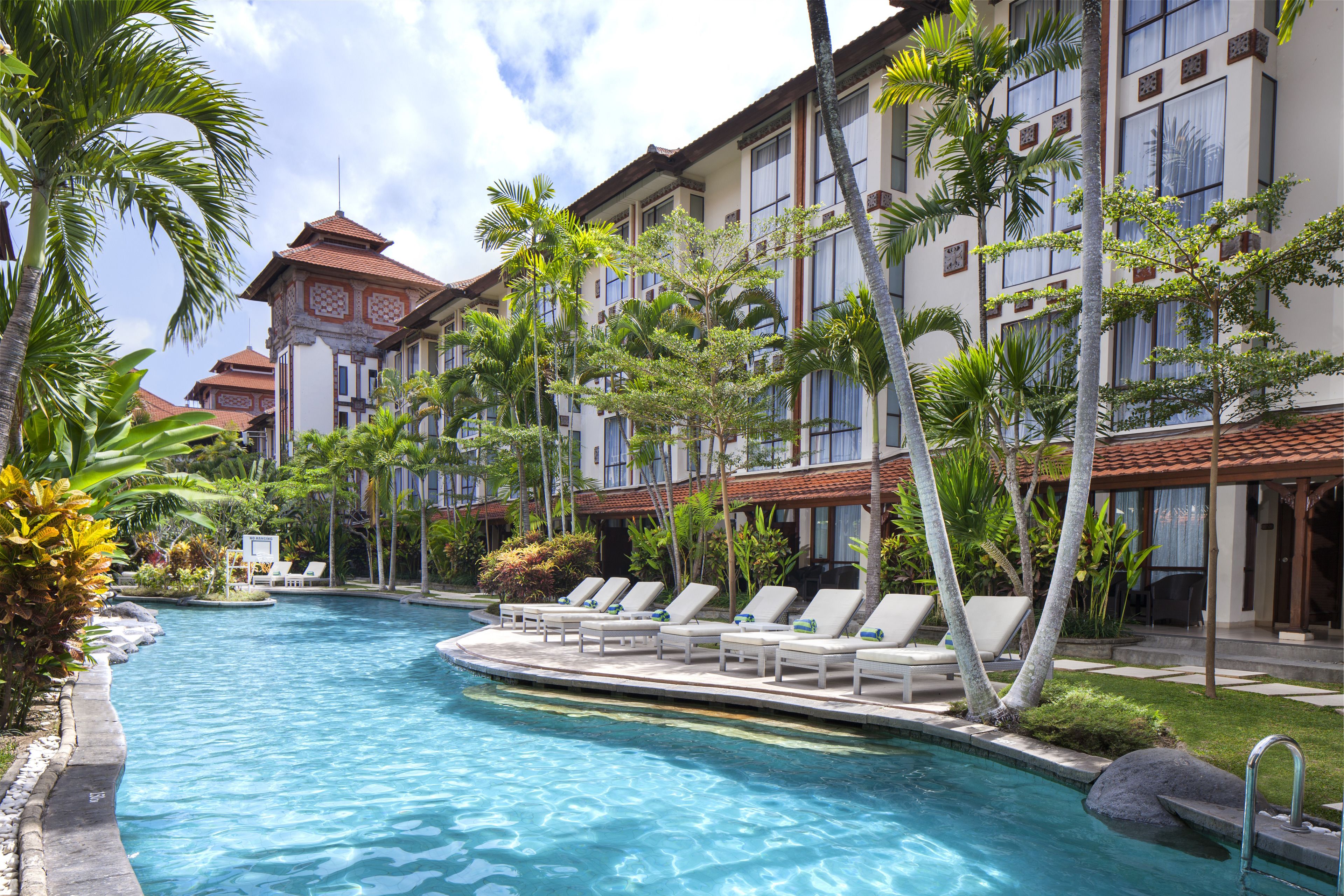 A hotel with a swimming pool, palm trees, and a traditional architectural style.