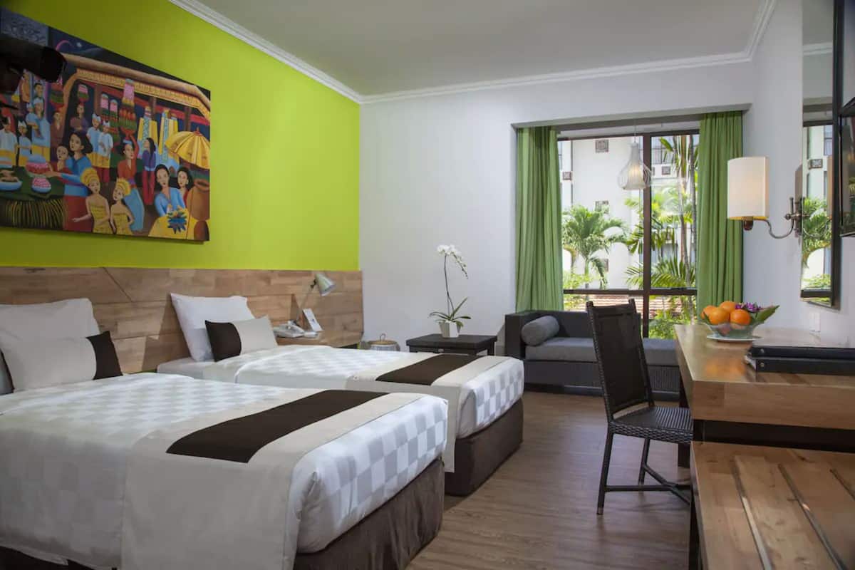 Een hotelkamer met twee bedden, een bureau, een stoel, een schilderij aan de muur en uitzicht op het landschap.