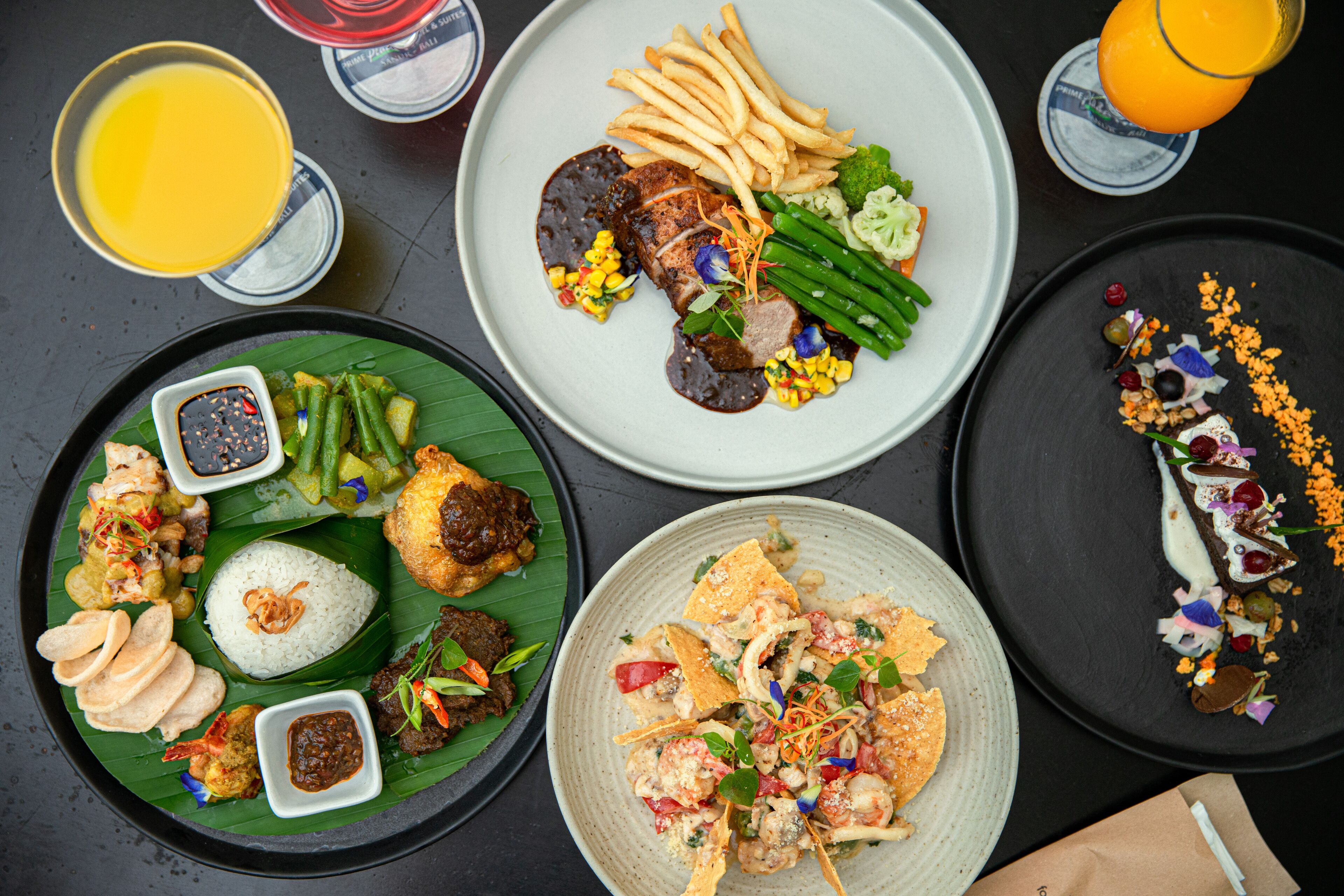 A variety of dishes on plates, including rice, vegetables, and meat, with drinks and condiments in the background.
