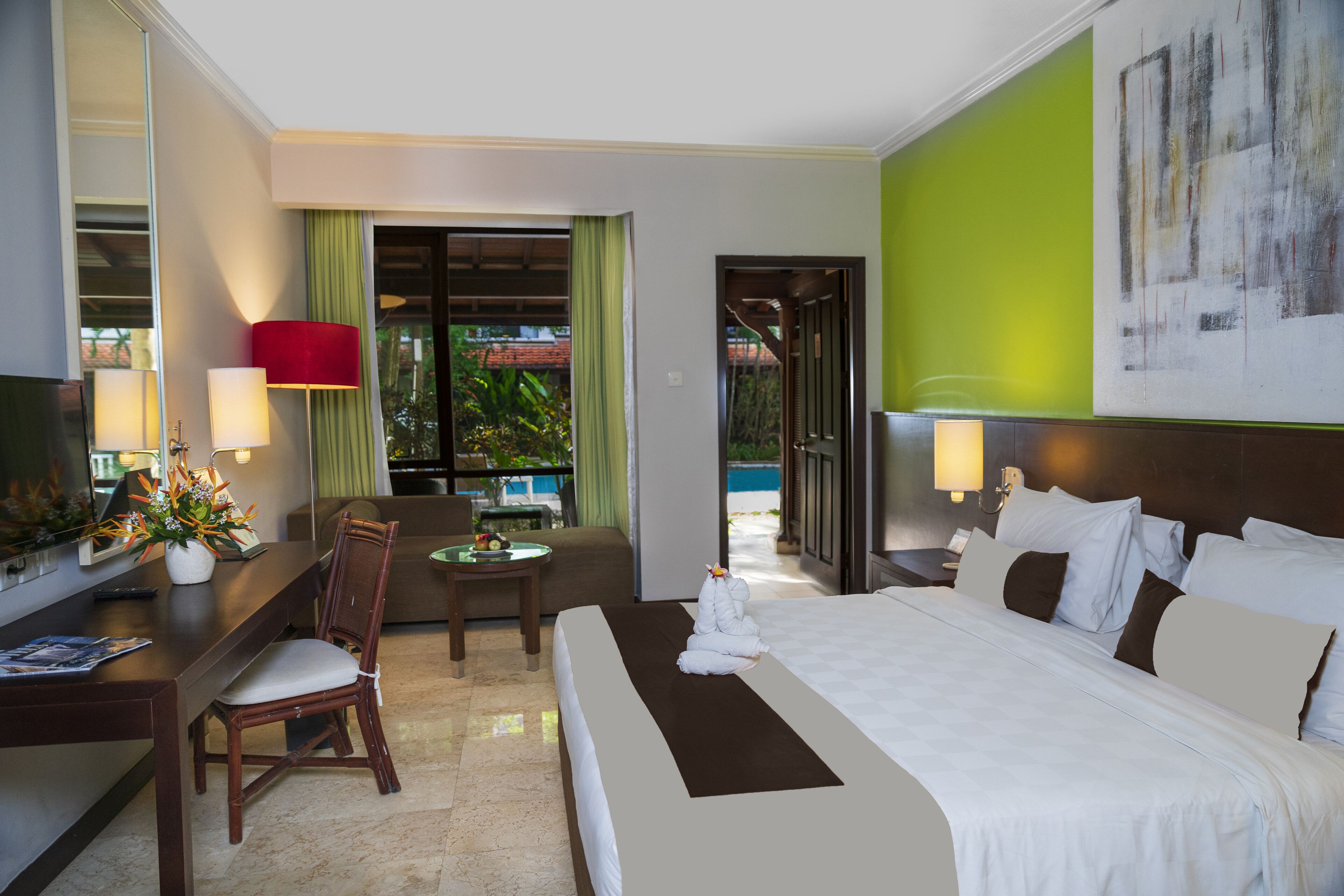 A hotel room with a bed, a desk with a lamp, a chair, and a view of a pool.