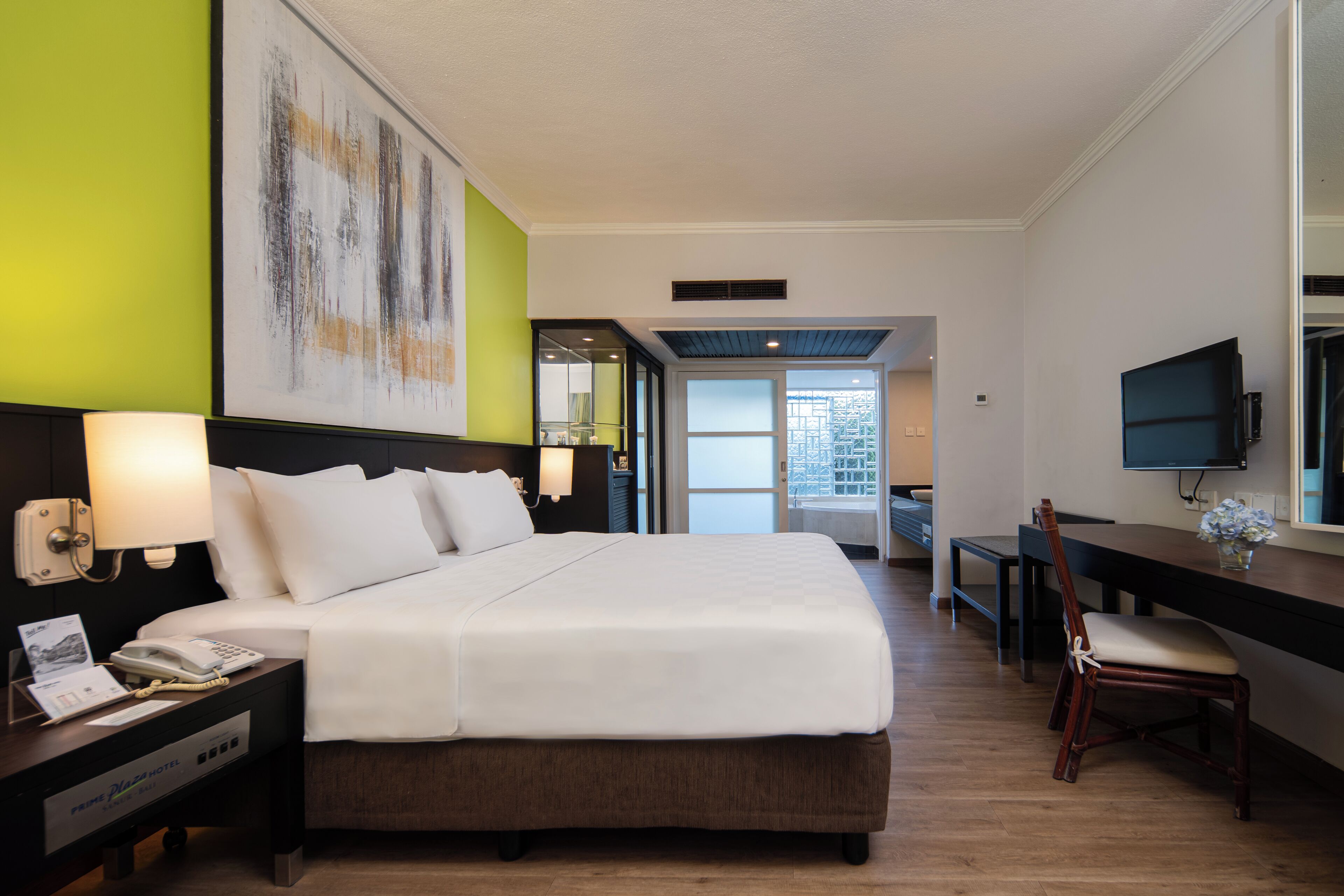Una camera d'albergo con un letto grande, comodini con lampade, una scrivania con una sedia, una televisione e un'ampia finestra.