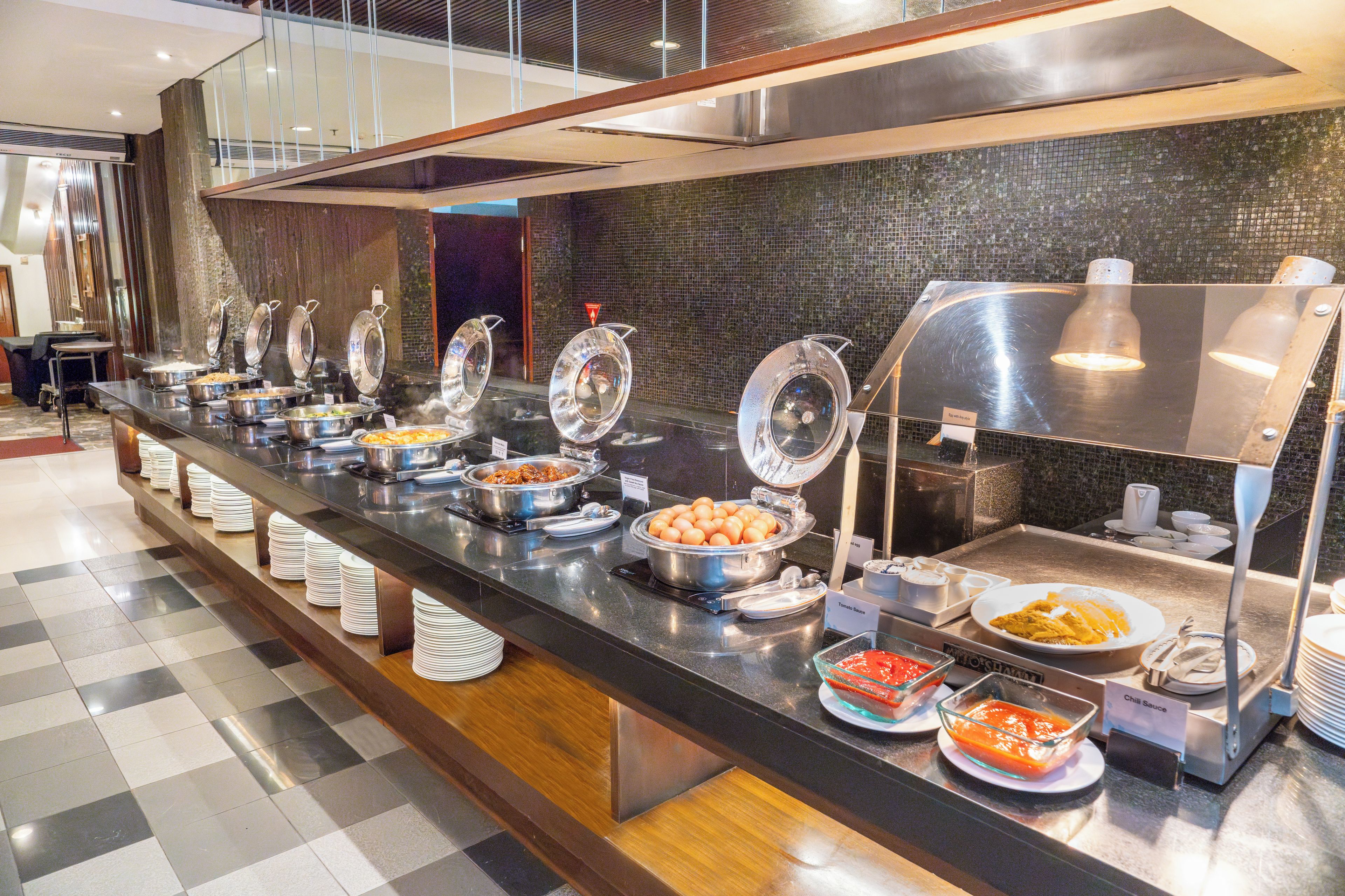 A buffet with various food stations including eggs, tomato sauce, and chili sauce.
