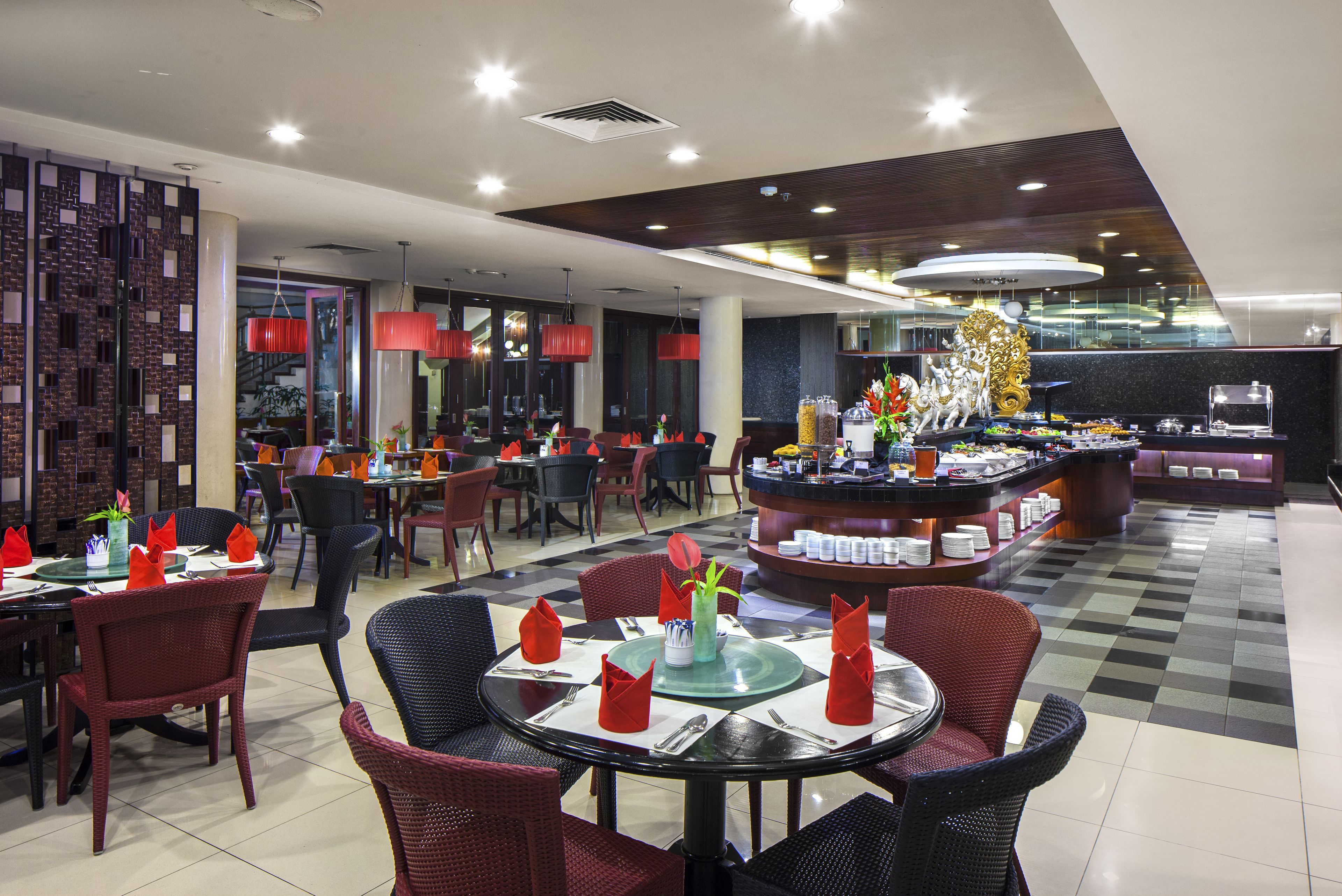 Un restaurant moderne avec des tables rondes, des serviettes rouges et une pièce décorative centrale.