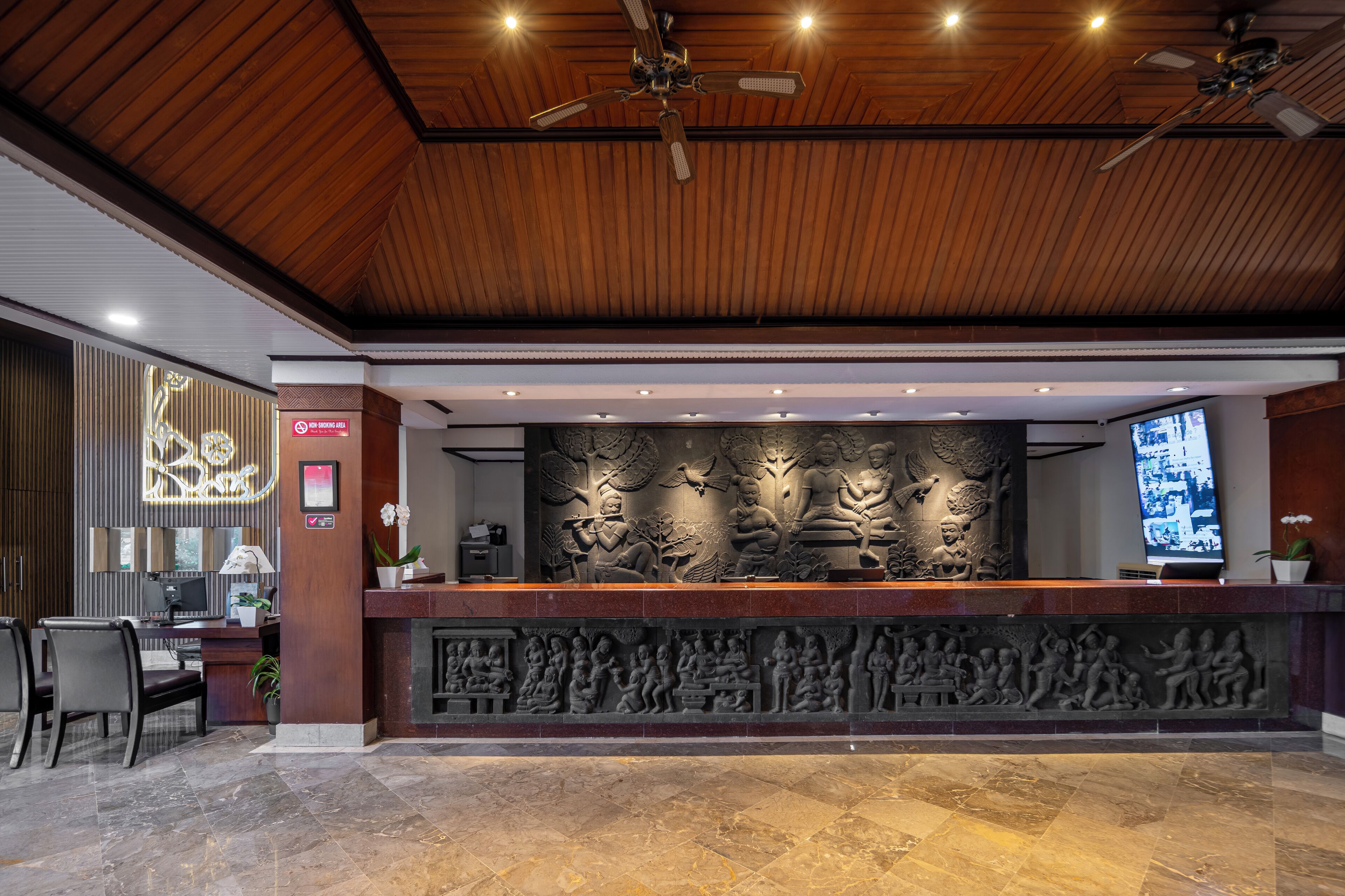 A reception area with a wooden ceiling, a marble reception desk, and a large wall sculpture.