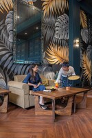 A room with a large mirror, a sofa, a wooden coffee table, and a decorative wall with leaf patterns.