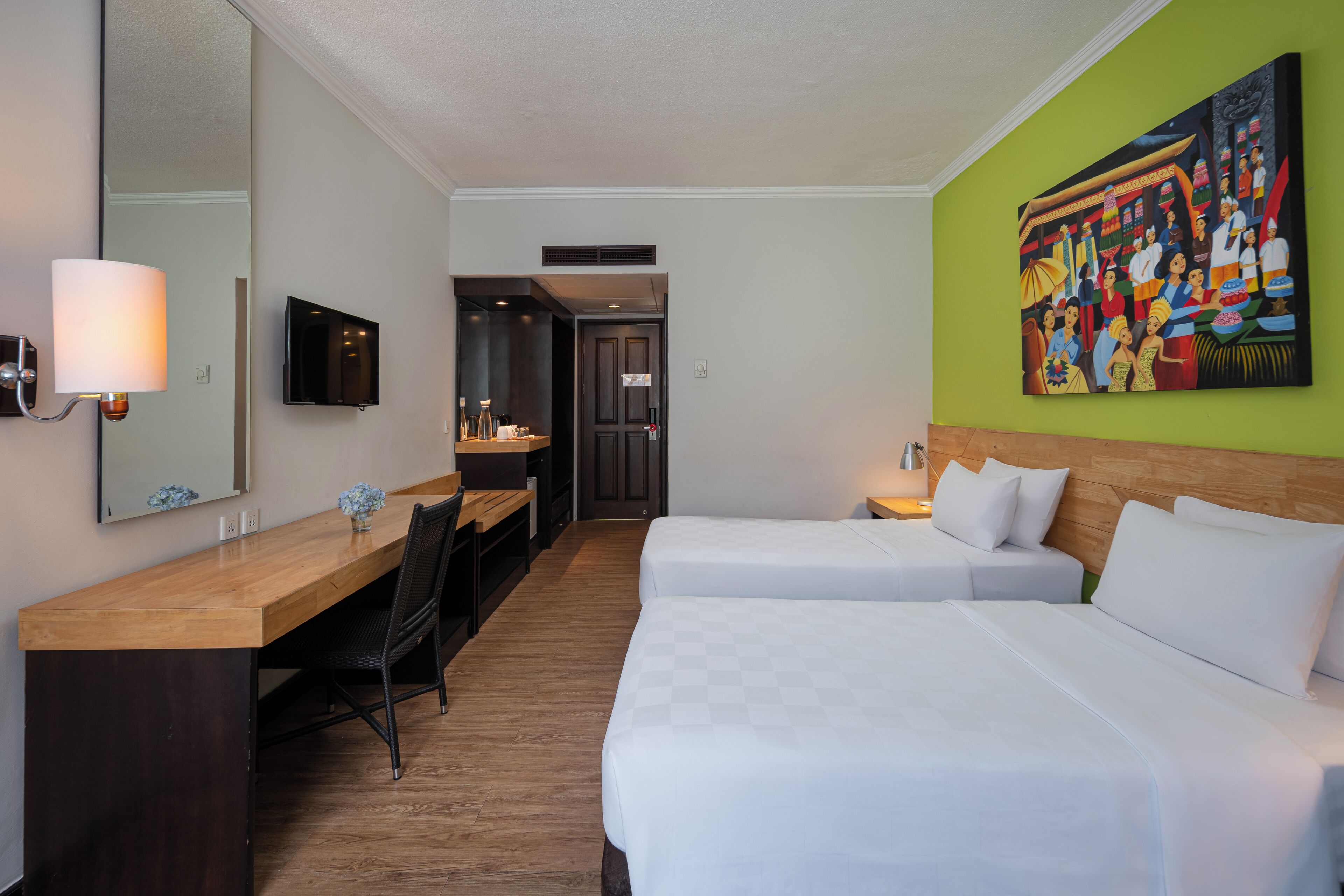 Een hotelkamer met twee bedden, een bureau, een stoel, een televisie en een groot schilderij aan de muur.