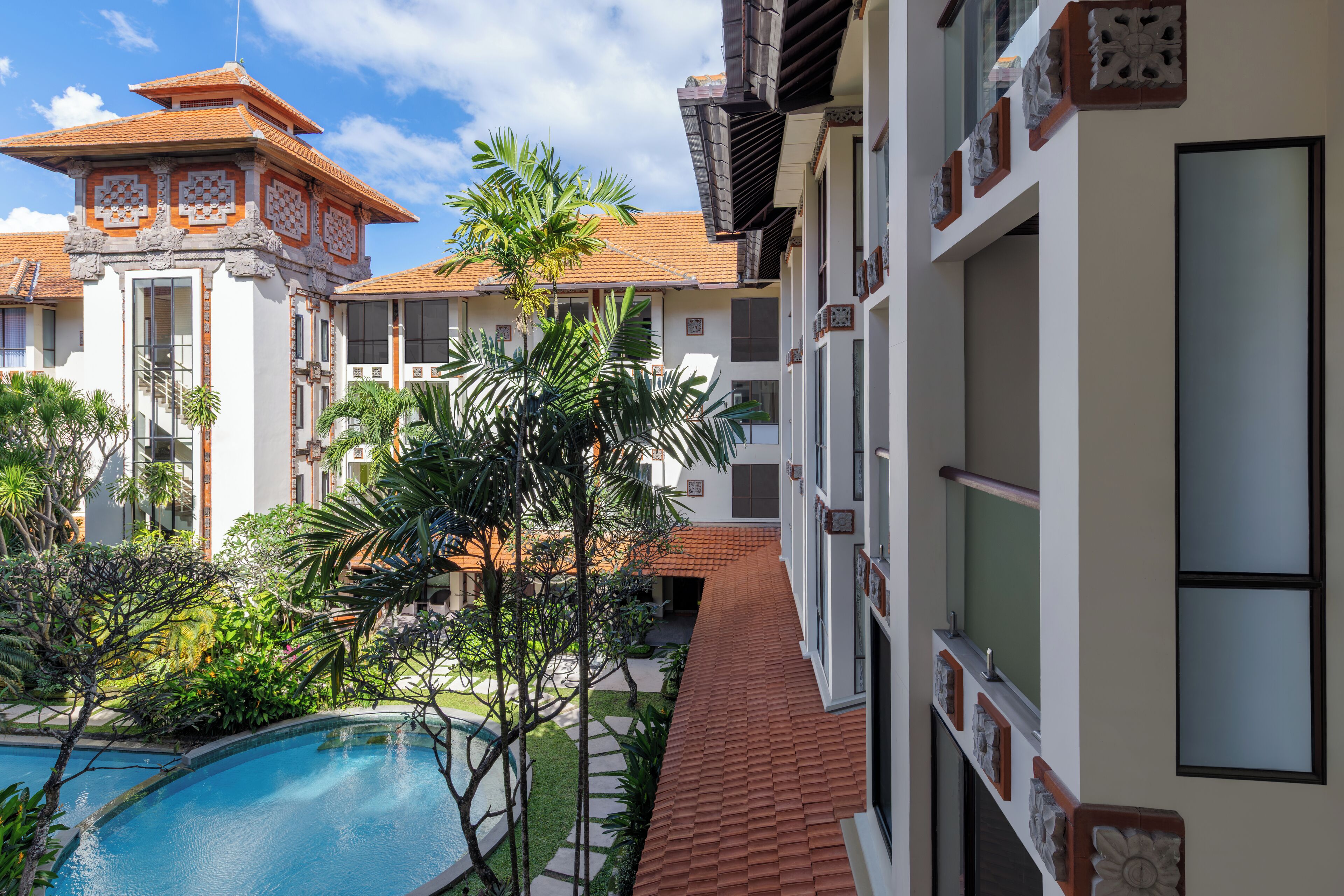 A hotel with a swimming pool surrounded by lush greenery and palm trees.