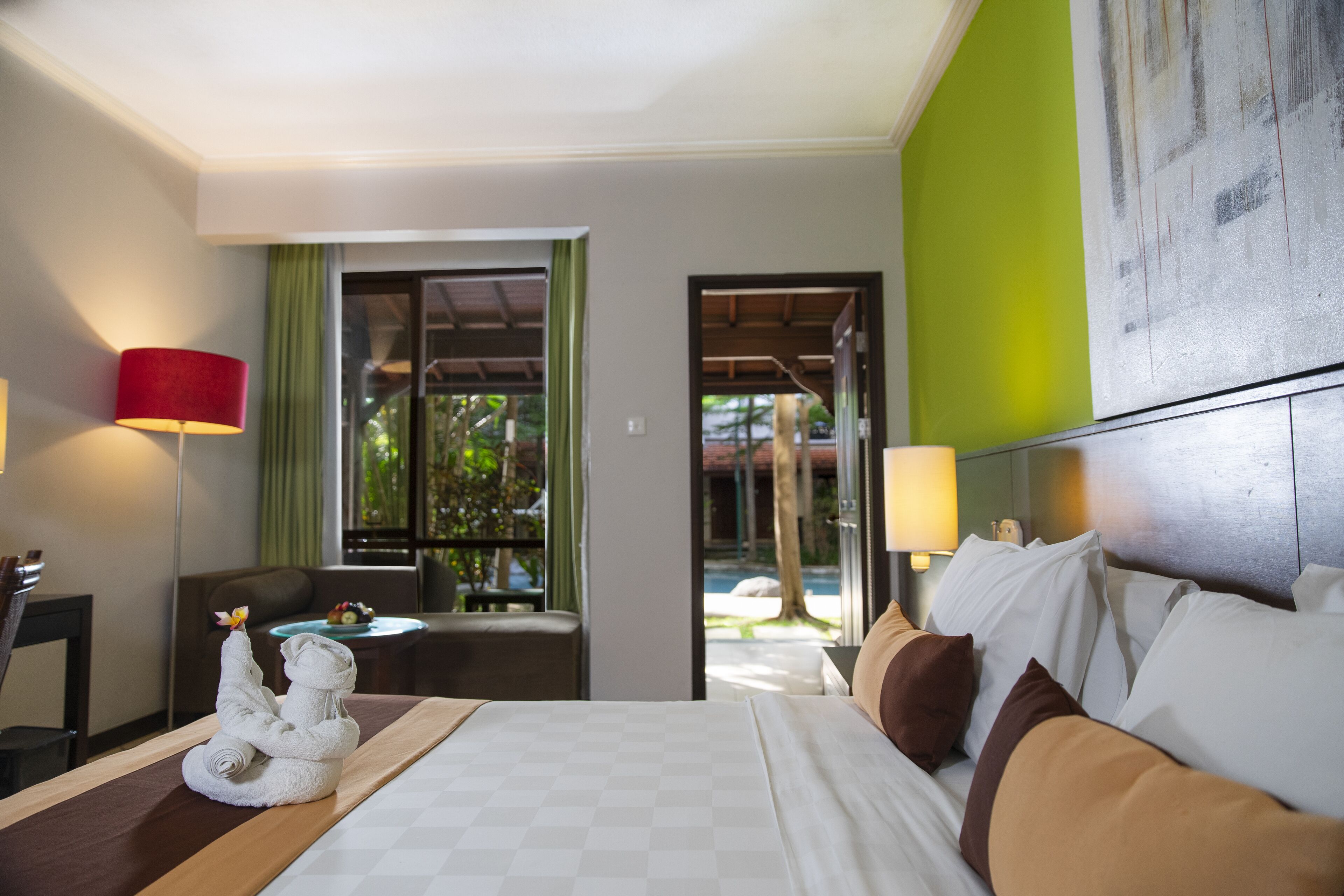 Habitación de hotel con cama, escritorio, silla, lámpara y vistas al exterior.