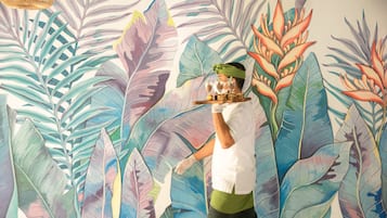 Una persona pinta un mural de hojas y flores tropicales.