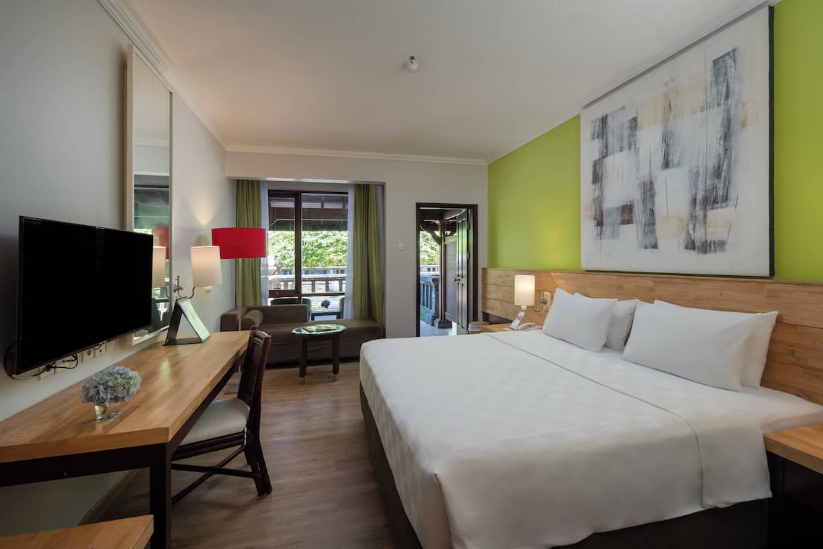 Een hotelkamer met een bed, een bureau met een televisie, een stoel, een tafeltje en een schilderij aan de muur.