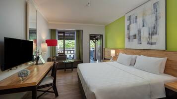 Ein Hotelzimmer mit einem Bett, einem Schreibtisch mit Fernseher, einem Sessel, einem kleinen Tisch und einem Bild an der Wand.