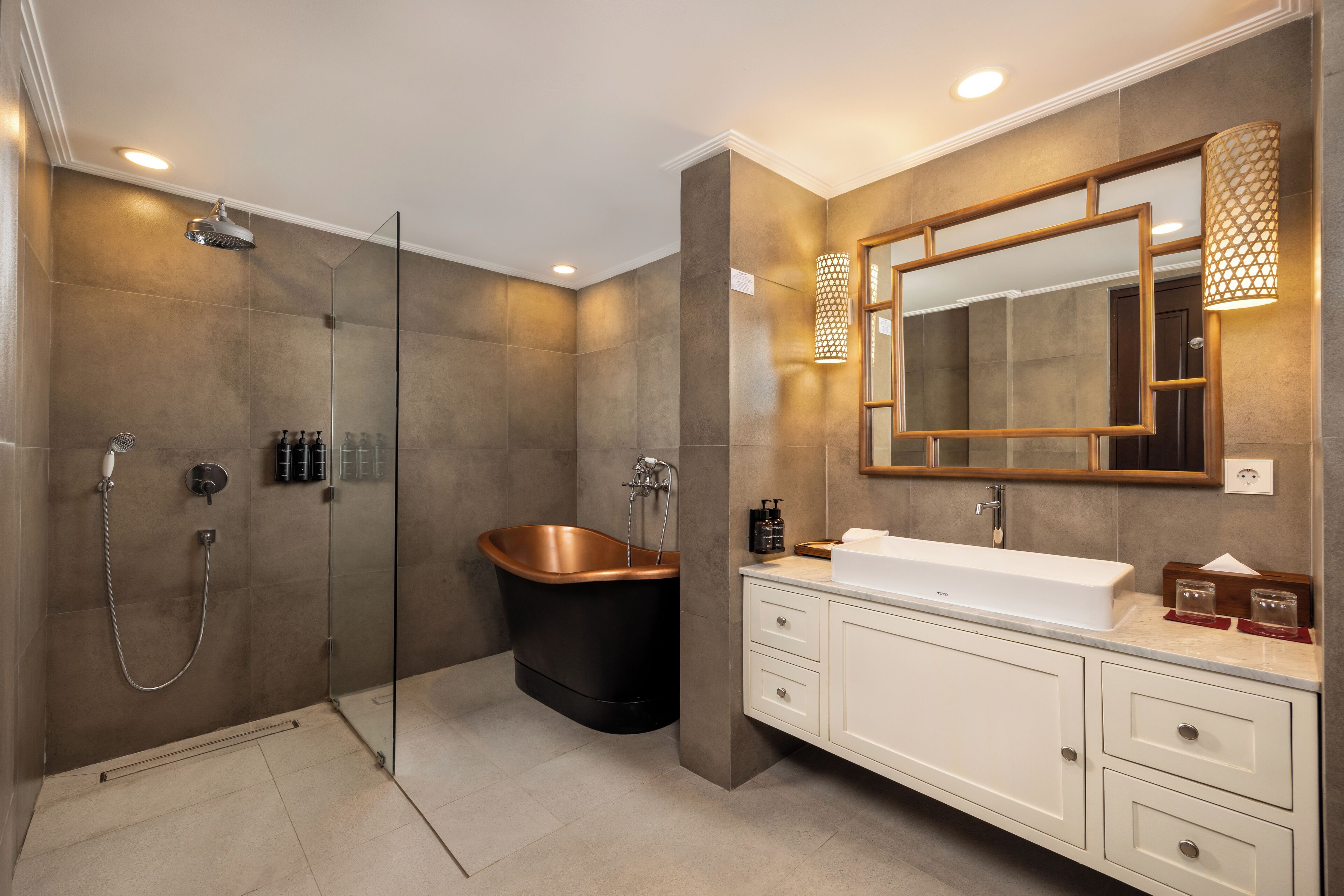 Un baño moderno con ducha envuelta en vidrio, una bañera independiente y un tocador con un espejo grande y apliques de luz.