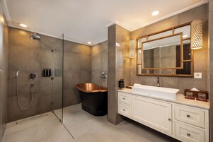 Un baño moderno con ducha envuelta en vidrio, una bañera independiente y un tocador con un espejo grande y apliques de luz.
