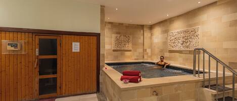 A spa area with a hot tub, wooden paneling, and stone walls.