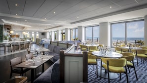 A restaurant with a bar area, seating arrangements, and large windows offering a view of the ocean. - Shoreline Hotel (Donabate)