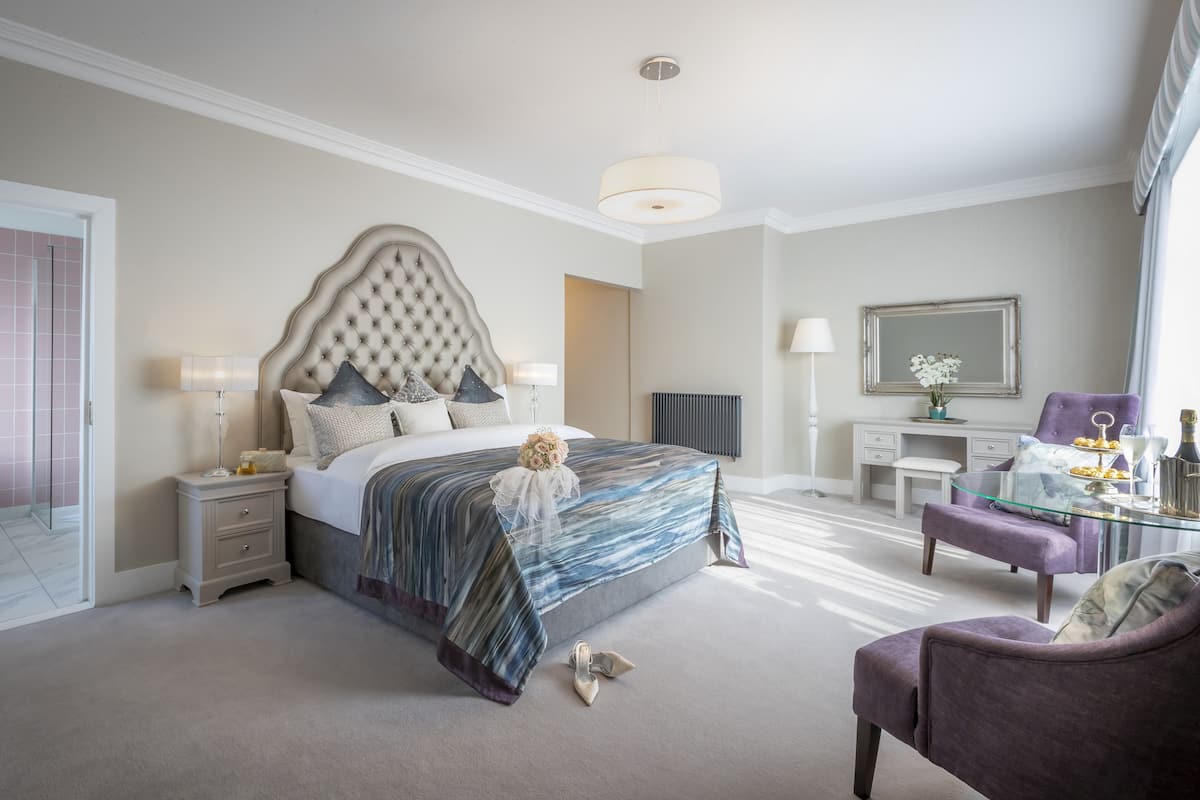 A bedroom with a large bed, a vanity, a chair, and a desk.