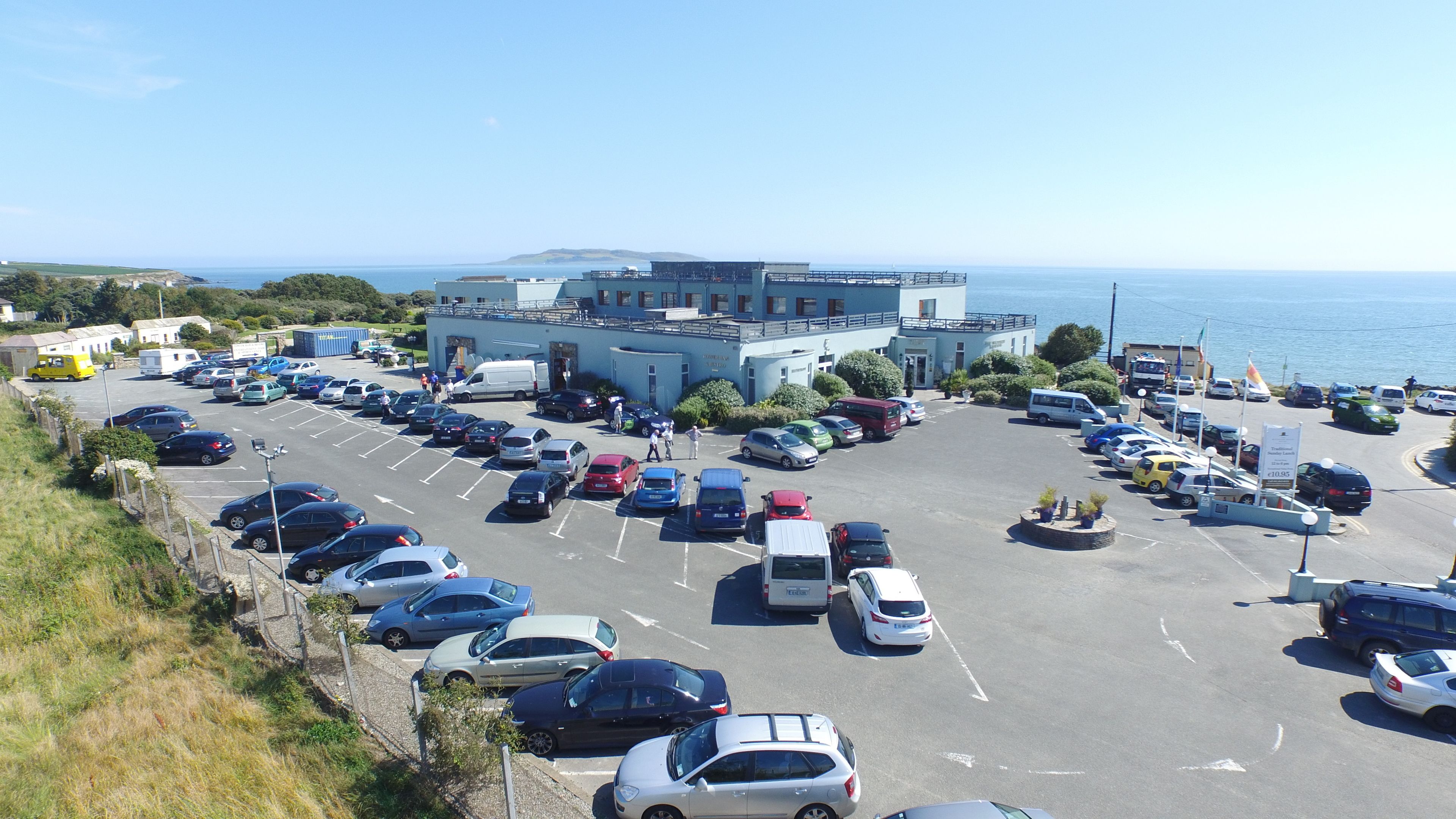 Ein Parkplatz mit mehreren Autos und einem Gebäude mit Blick auf das Meer.