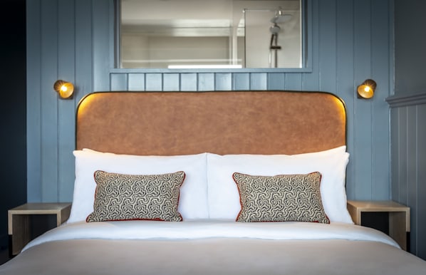 A neatly made bed with a patterned headboard and pillows, two bedside tables, and a mirror above the bed. - Shoreline Hotel (Donabate)