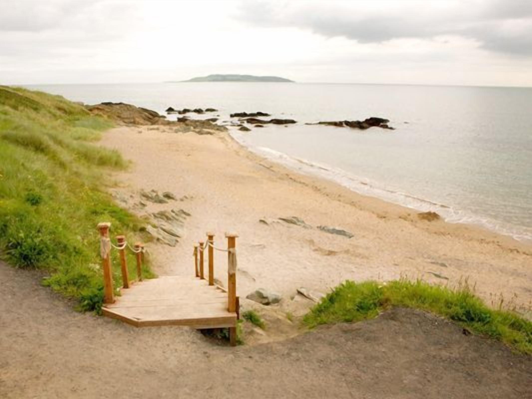 Un sendero de madera que conduce a una playa con vista al mar y a la costa distante.