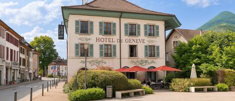 A hotel with a sign reading 'HOTEL DE GENEVE' and a terrace with outdoor seating.