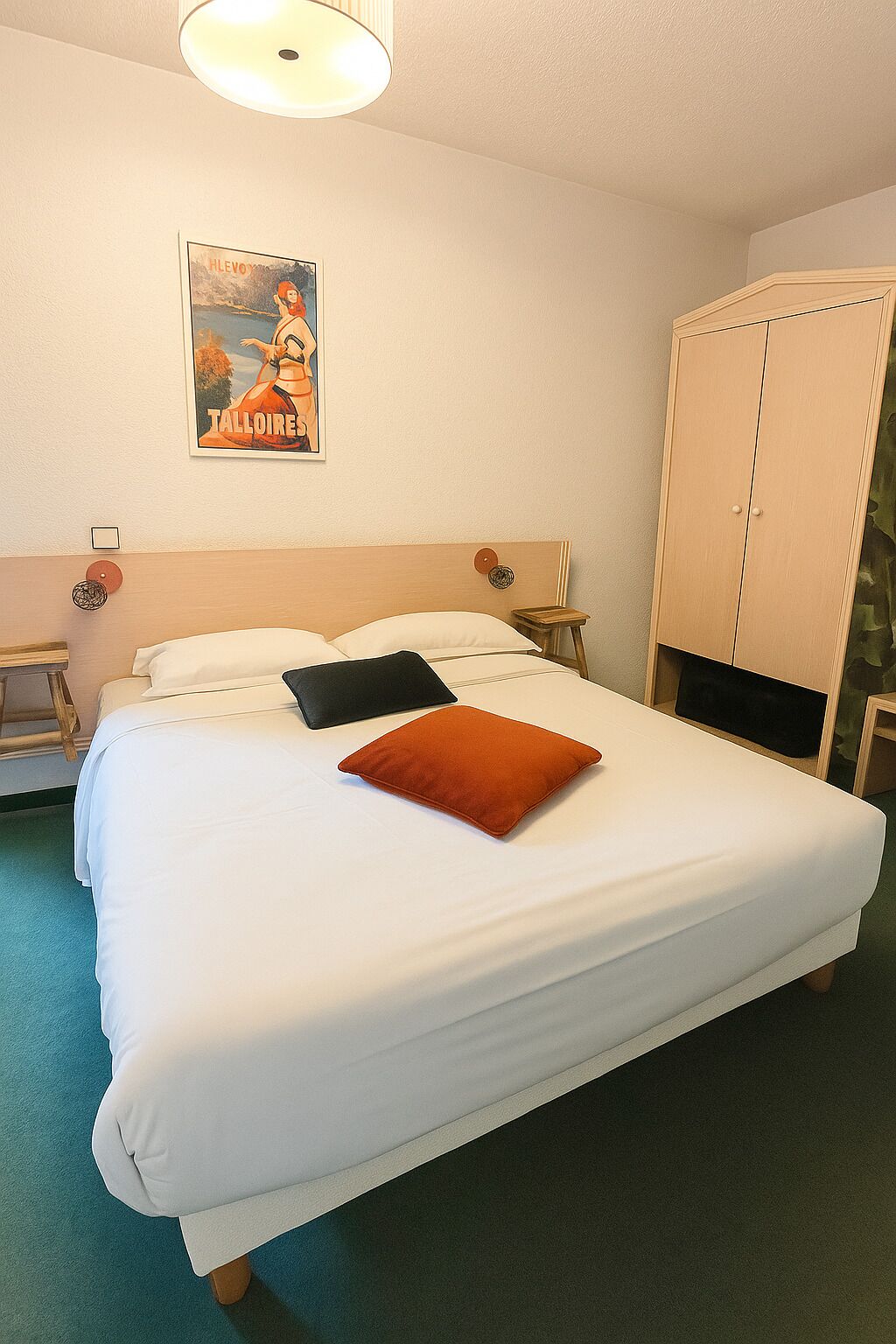 Un letto rifatto con lenzuola bianche e un cuscino arancione, un comodino in legno con una lampada, un armadio e un quadro appeso al muro.