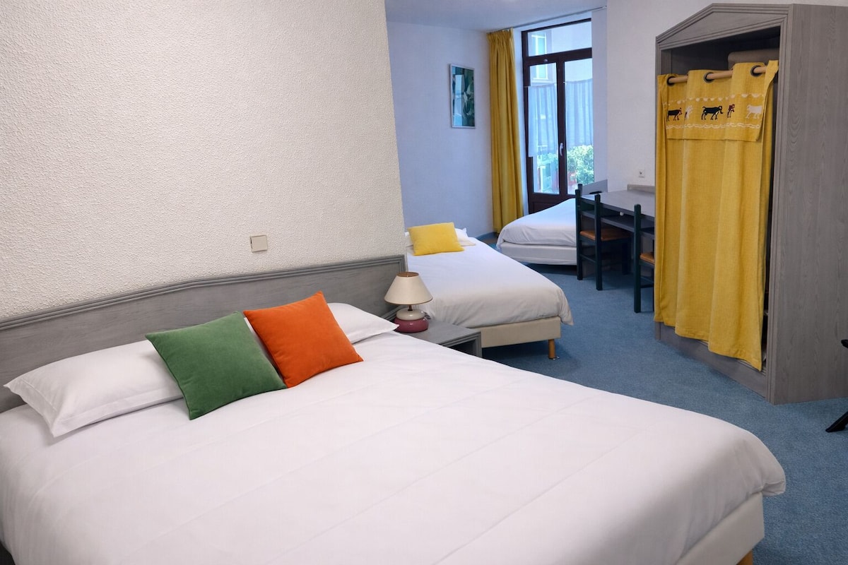 Ein Hotelzimmer mit zwei Betten, einem Schreibtisch und einem Fenster mit gelben Vorhängen.