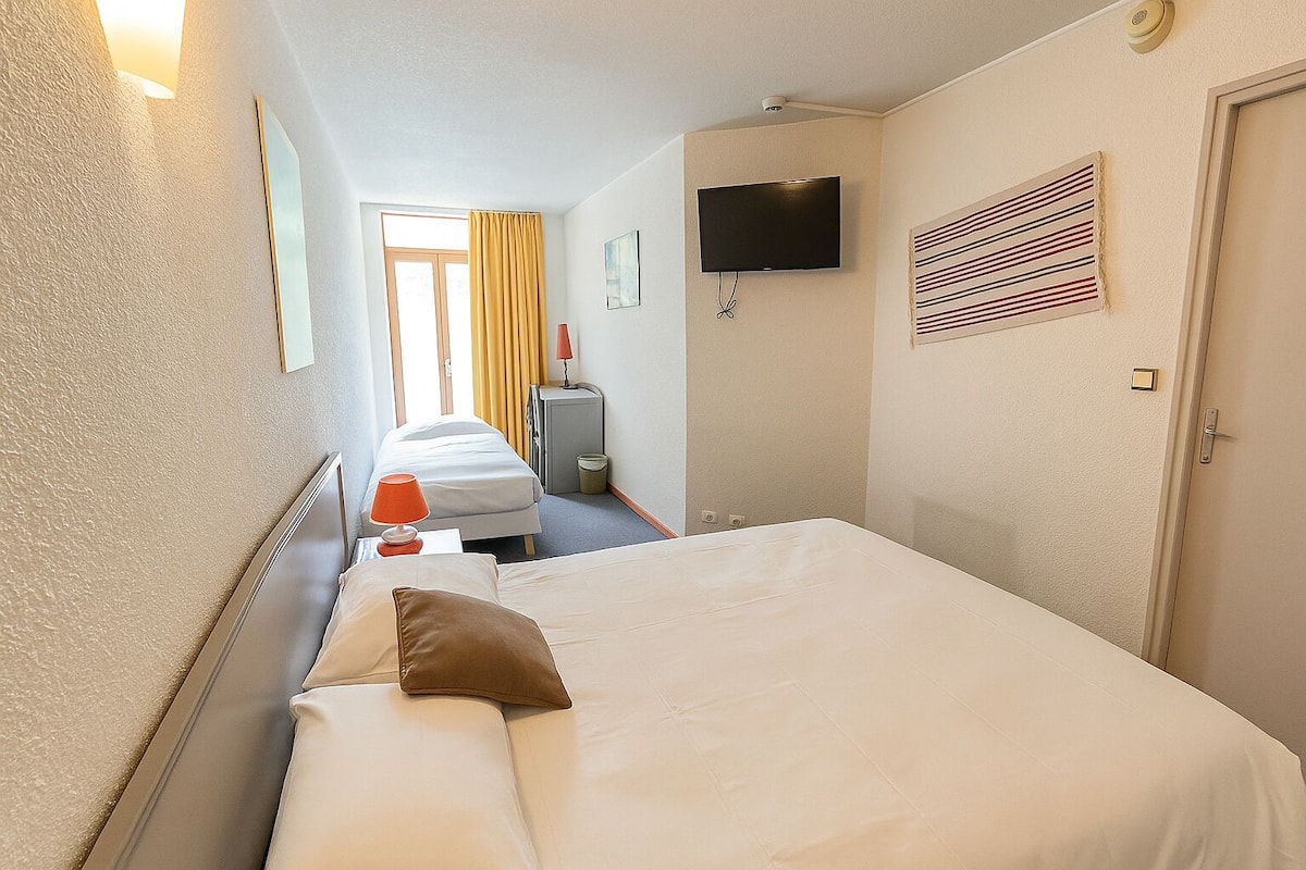 Ein Hotelzimmer mit Bett, Fernseher, einem Fenster mit Vorhängen, einer Tür und einer Wand-Klimaanlage.