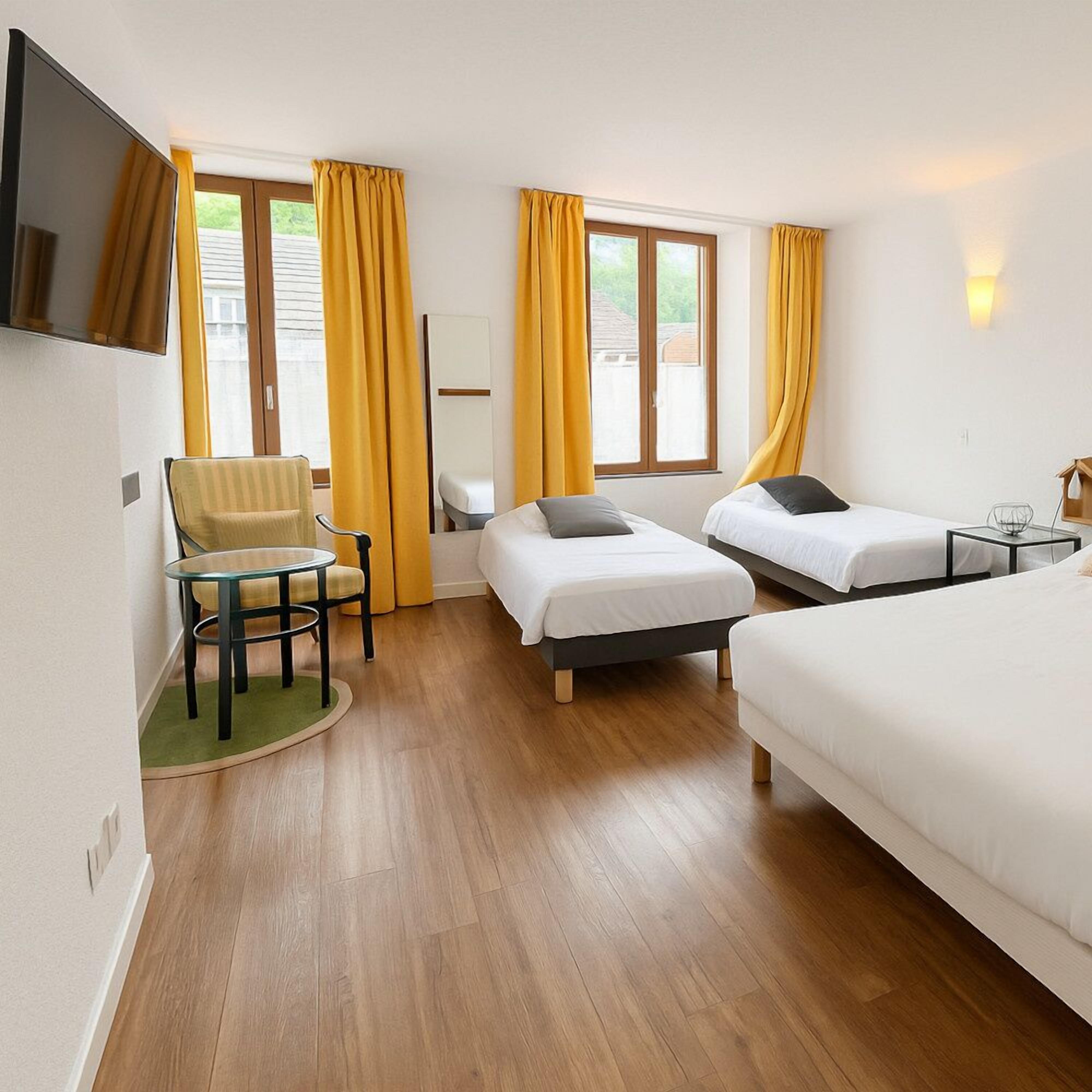 Une chambre d’hôtel avec deux lits simples, un canapé-lit, une petite table, une chaise et un téléviseur.