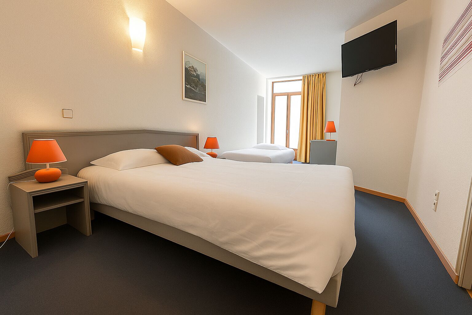Una habitación de hotel con una cama grande, dos mesitas de noche con lámparas, un televisor de pantalla plana en la pared y un ventanal con cortinas.