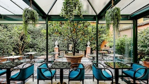 Un jardin intérieur aménagé avec des tables et des chaises, entouré d’une végétation luxuriante et d’orangers.