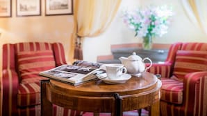 Une table en bois, sur laquelle se trouvent une théière, une tasse et un magazine, entourée de canapés à rayures, et des tableaux encadrés ornent le mur.