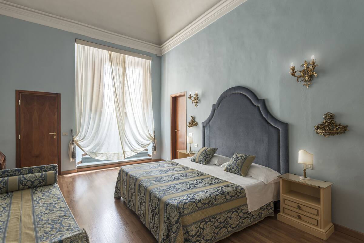 A bedroom with a large bed, a nightstand, a chair, and a window with curtains.