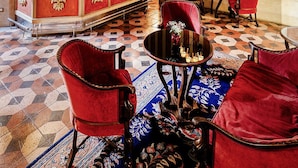 Un hall d’entrée luxueux avec un sol à carreaux, des fauteuils à revêtement rouge, une table centrale et un lustre décoratif.