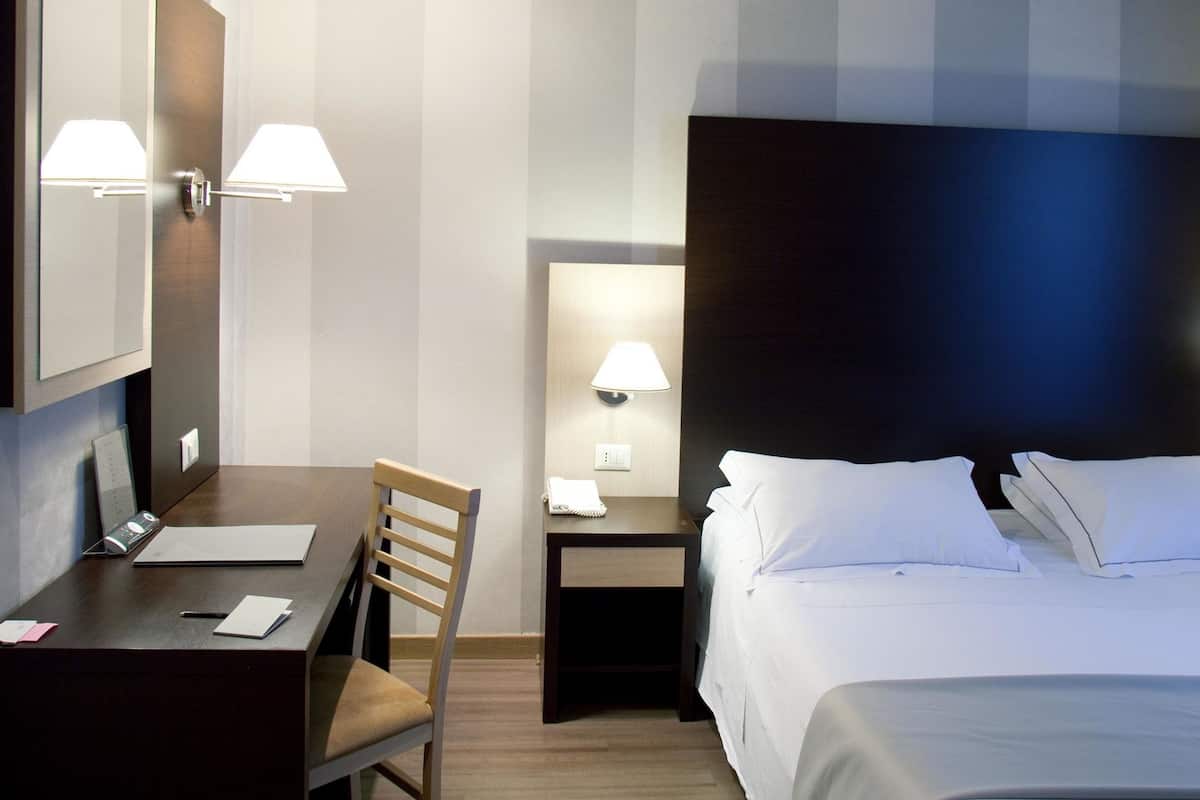 A hotel room with a bed, desk, chair, and nightstands.